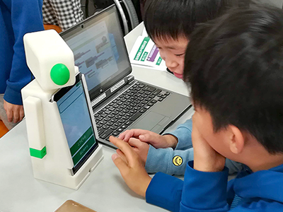 ノートパソコンの動画を見ながらロボットこくりを操作する子どもたち
